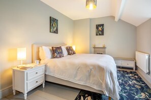 A bedroom with a bed, bedside tables, a nightstand, a lamp, a fireplace, and artwork on the walls. - 3 Bed in Islawrdref (oc-t34600) (Islawr-dref)