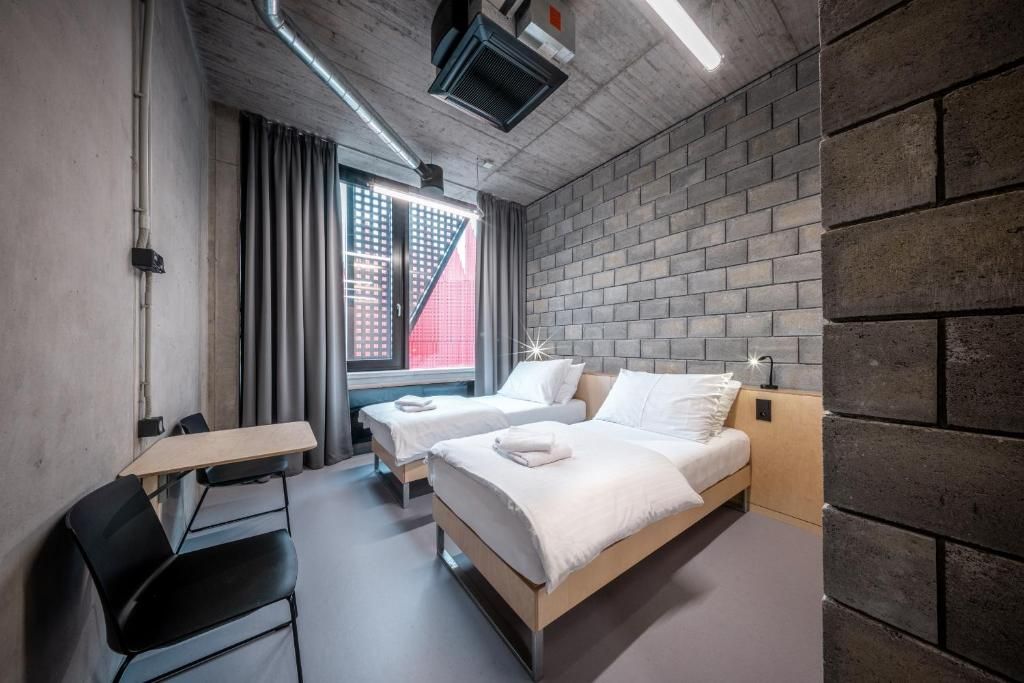 A modern hotel room with a brick wall, two beds, a desk, and a chair.