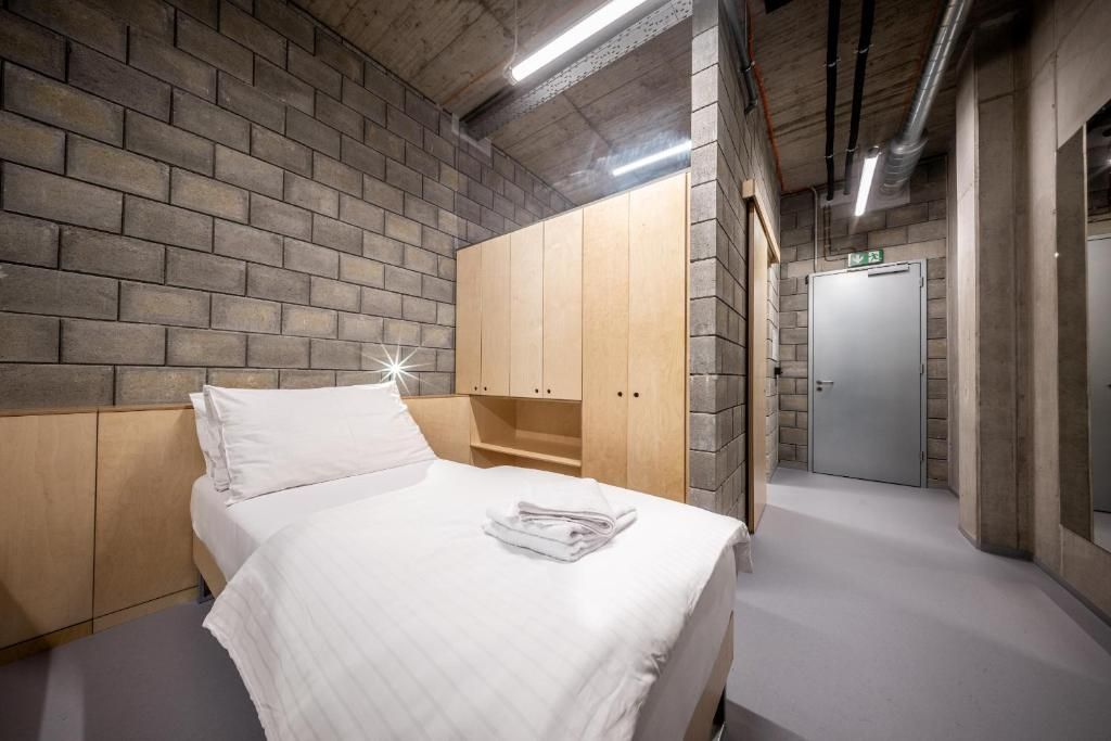 A hotel room with a brick-patterned wall, a bed with white bedding, wooden cabinets, and a door leading to a hallway.