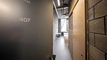A hallway with a number '407' on the wall, a wooden door on the right, and a view into a room with a bed and a window.