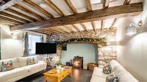 A cozy living room with a stone fireplace, wooden beams, a flat-screen TV, and a sofa with floral cushions. - 4 Bed in Ganllwyd (oc-g34601) (Ganllwyd)