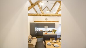 A modern kitchen with dark cabinets, a central island with a vase of flowers, and a dining area with a table set for two. - 4 Bed in Ganllwyd (oc-g34601) (Ganllwyd)