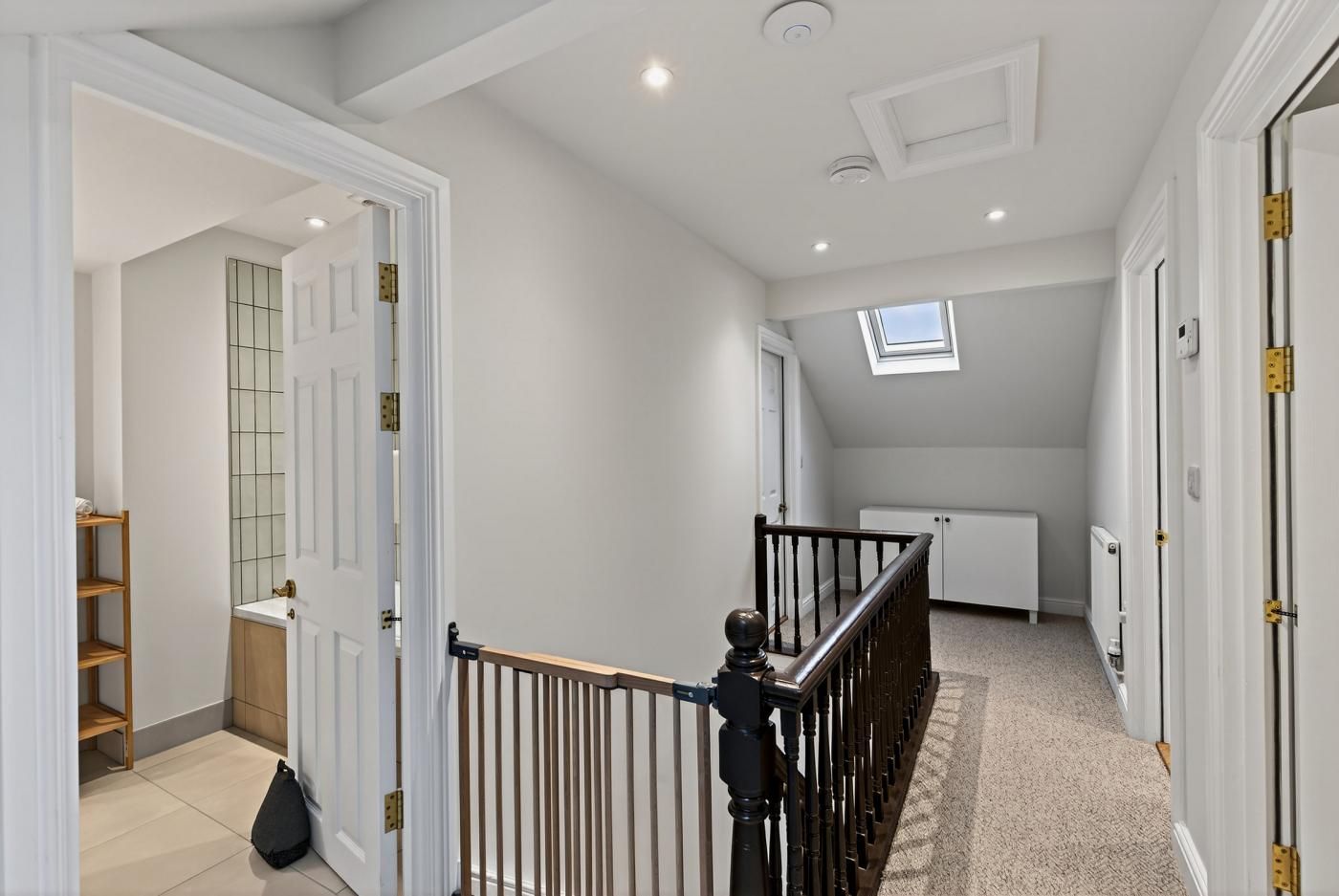 A spacious hallway with a wooden staircase, a skylight, and a radiator.