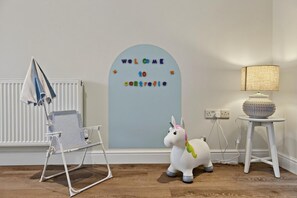 A room with a white radiator, a folding chair, a lamp on a small table, and a wall sign that reads 'WELCOME TO CARTERVILLE.' - 3 Bed in Aberdovey (oc-c33725) (Aberdovey)