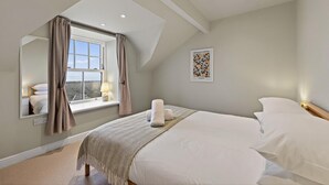 Quarto com uma cama grande, janela com cortinas, luminária de cabeceira e quadro na parede.