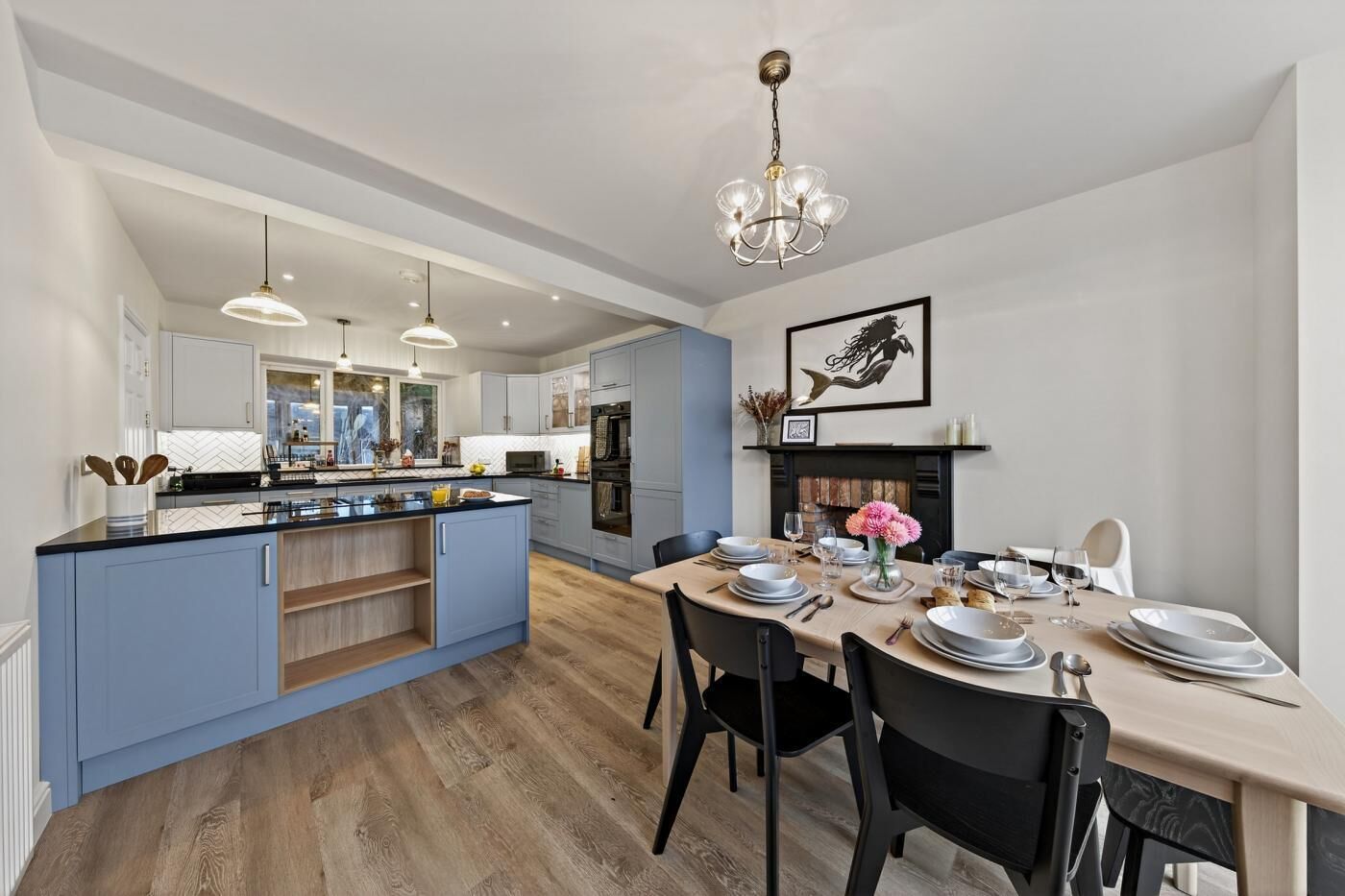 A modern kitchen with a central island, pendant lighting, and a dining area set for a meal.