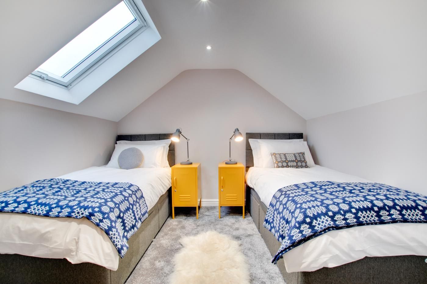 A bedroom with two beds, a skylight, and a small yellow cabinet.