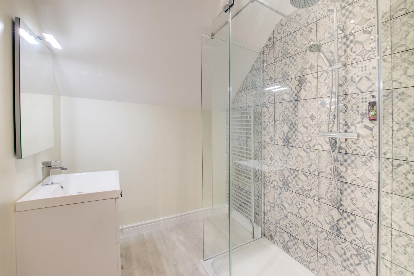 A modern bathroom with a glass-enclosed shower, a white sink, and patterned tiles.