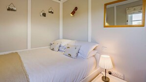 Ein Schlafzimmer mit Bett, Kissen, einer Nachttischlampe, einem Spiegel und Bilderrahmen an der Wand.
