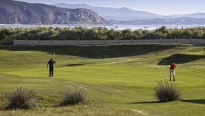 En golfbane med frit udsyn til havet og bjergene i baggrunden.