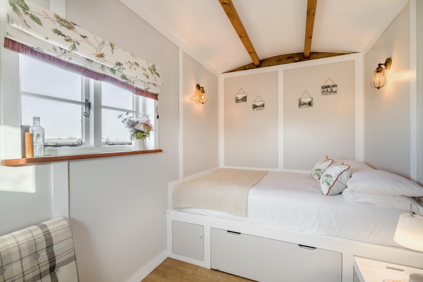 A bedroom with a bed, a window with curtains, wall-mounted lights, and a small shelf with items.