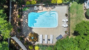 Vista aérea de una piscina con sillas de descanso y una pequeña zona de terraza rodeada de vegetación.