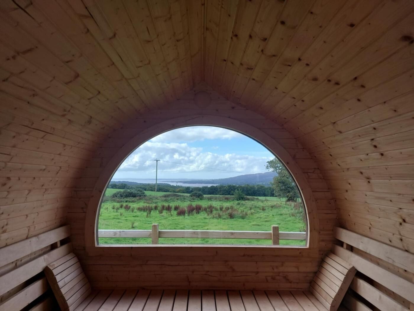 A wooden arched window with a view of a green landscape and distant hills.