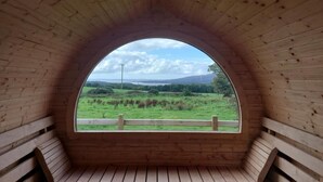 Una ventana arqueada de madera con vistas a un paisaje verde y colinas lejanas.