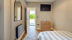 Une chambre à coucher comprenant un lit, une commode en bois, un téléviseur fixé au mur et une porte donnant sur un balcon.