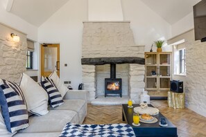 A cozy living room with a stone fireplace, a sofa with striped cushions, a coffee table with breakfast items, and a bookshelf. - 2 Bed in Nantgaredig (oc-t34635) (Llanarthney)