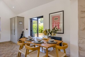 Un comedor con una mesa de madera preparada para cuatro personas, rodeada de sillas de mimbre. Un cuadro con la palabra 'LOVE' está en la pared.