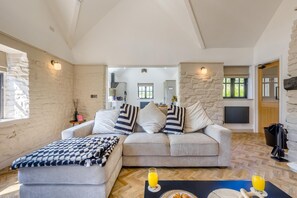 Una sala de estar con sofá, reposapiés y una mesa de centro con bebidas. Se ve una cocina al fondo.