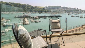 Ein Balkon mit zwei Stühlen und einem kleinen Tisch, mit Blick auf einen Hafen voller Boote und eine ferne Stadt.