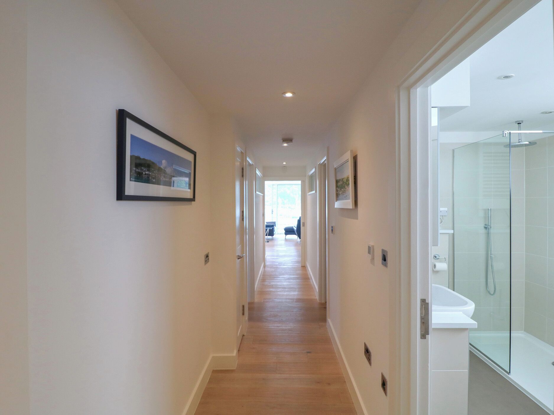 A hallway with framed pictures, a glass shower enclosure, and a view into another room.