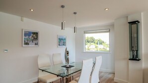 Ein Essbereich mit Glastisch und weißen Stühlen, ein Fenster mit Ausblick und ein Thermometer an der Wand.