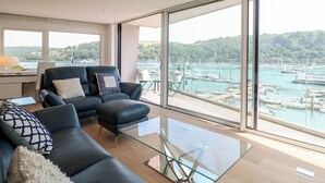 Ein modernes Wohnzimmer mit einem Glastisch, einem schwarzen Ledersofa und Blick auf eine Marina.