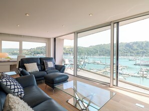 Ein modernes Wohnzimmer mit einem Glastisch, einem schwarzen Ledersofa und Blick auf eine Marina.
