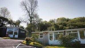A small, single-story building with a large window, surrounded by greenery and trees.