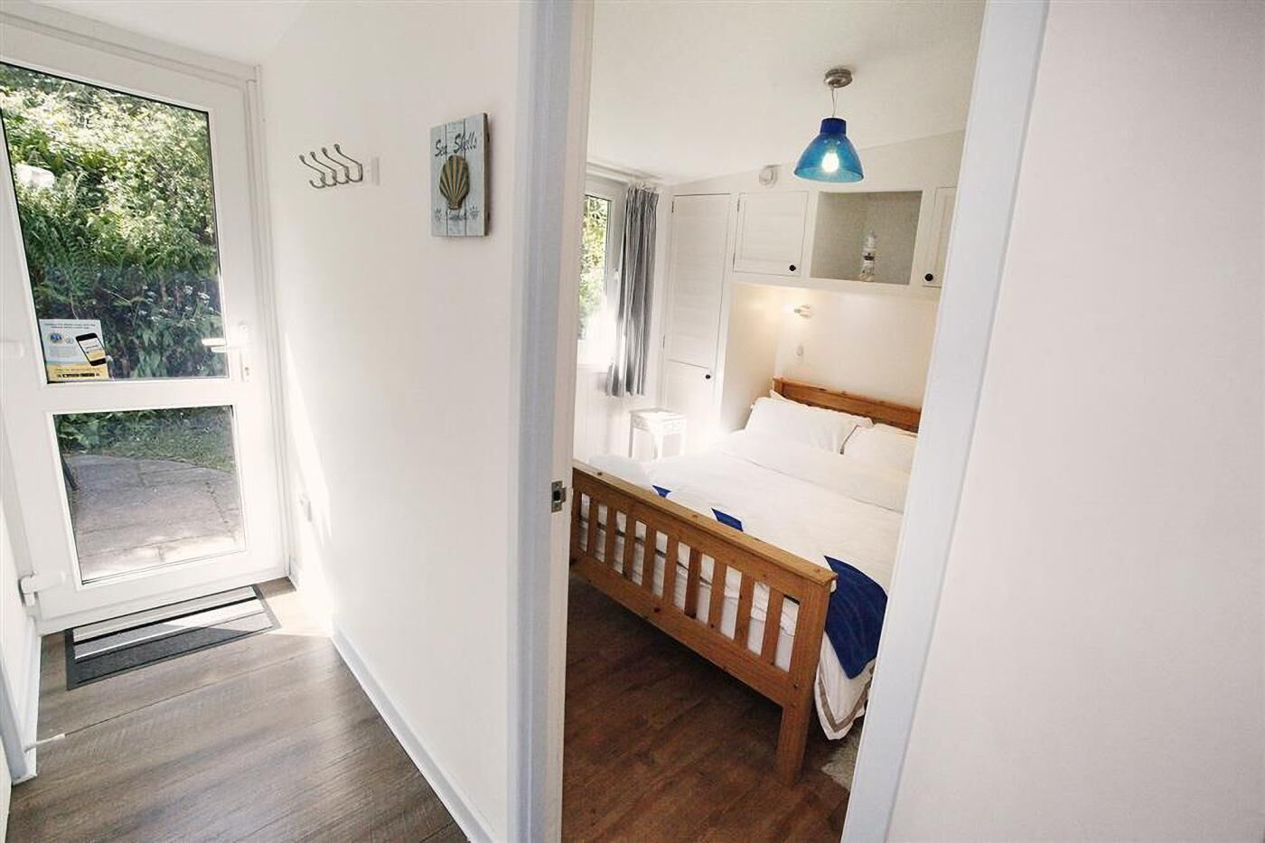 A bedroom with a wooden bed, a blue pendant light, and a view of the outdoors through a door.