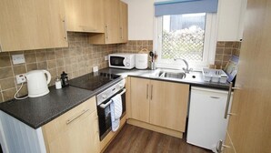 A compact kitchen with a microwave, kettle, oven, and sink.