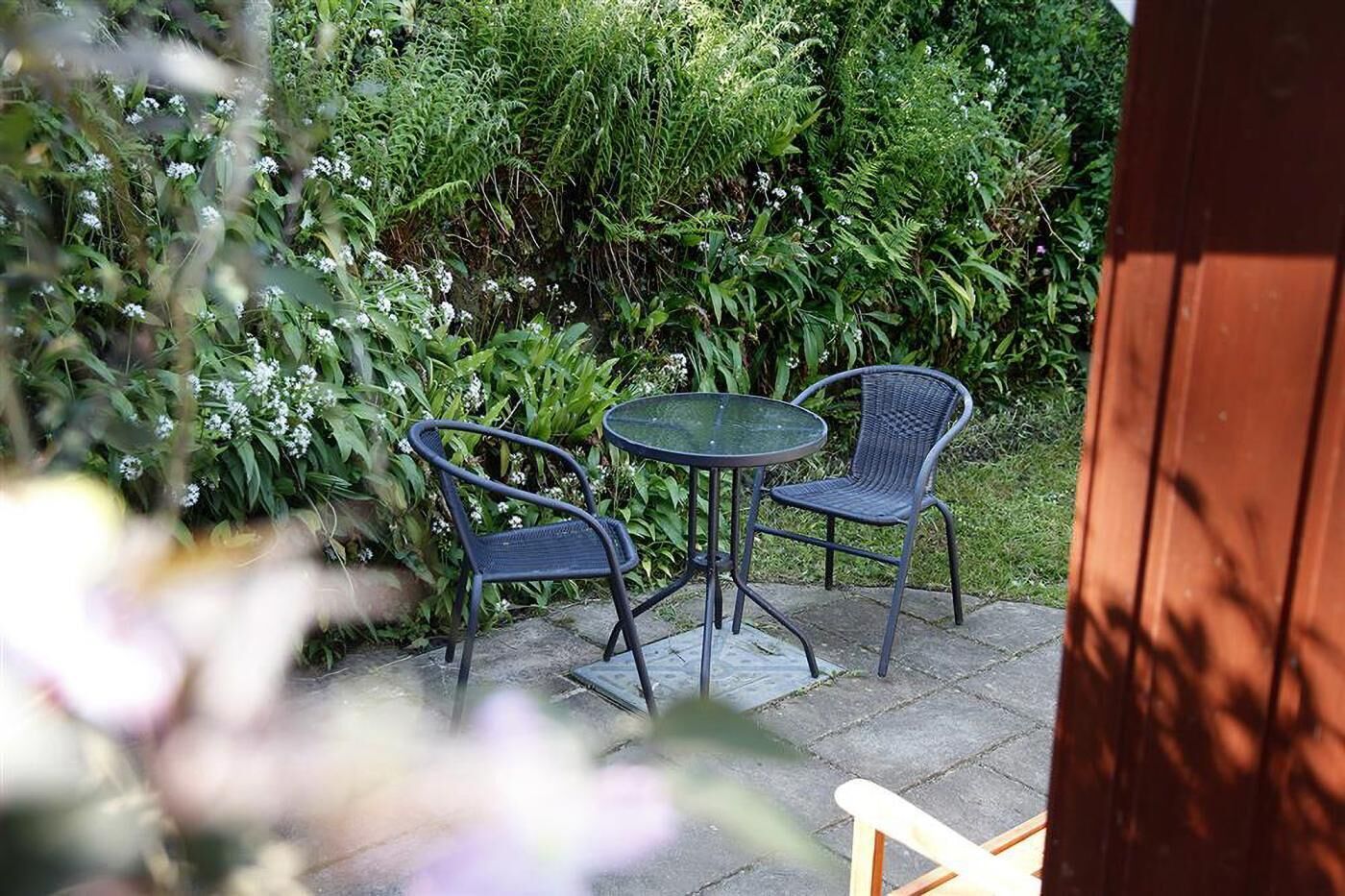 Une terrasse extérieure avec deux chaises et une table, entourée d’une végétation luxuriante.