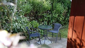 An outdoor patio with two chairs and a table, surrounded by lush greenery.