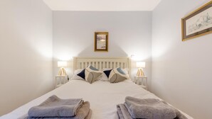 Een opgemaakt bed met kussens, twee nachtlampjes en opgevouwen handdoeken.