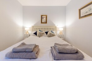 Ein ordentlich bezogenes Bett mit Kissen, zwei Nachttischlampen und gefalteten Handtüchern.