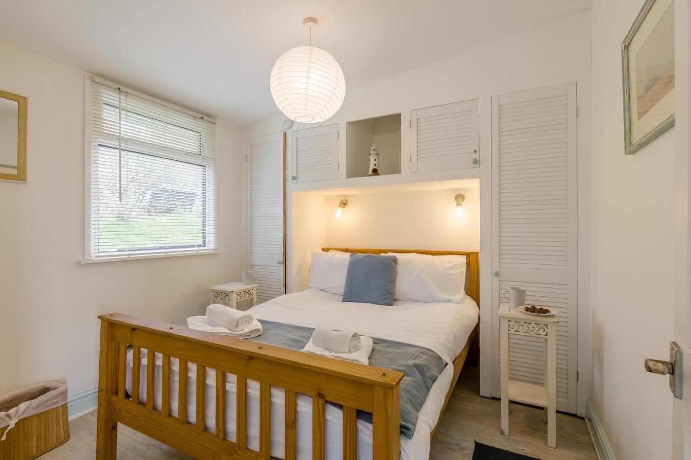 A bedroom with a bed, bedside tables, a hanging light fixture, and a window with blinds.