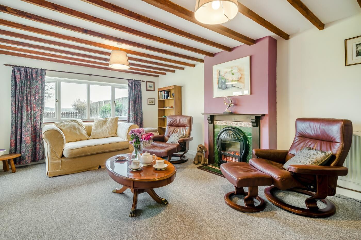 A cozy living room with a sofa, two leather chairs, a wooden coffee table, a fireplace, and a bookshelf.
