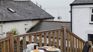 Een houten terras met een gedekte tafel, met uitzicht op een woongebied met huizen en een waterpartij.