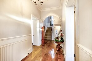Un couloir avec un plancher en bois, des murs blancs, un escalier et une petite table sur laquelle se trouve un vase.