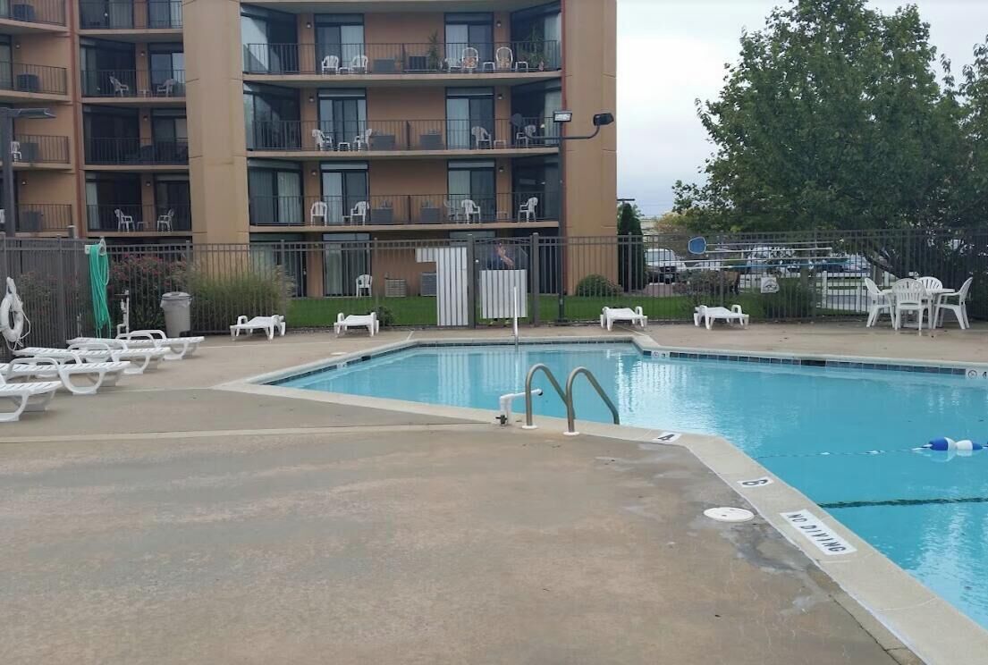 Une piscine avec des chaises longues et, en arrière-plan, un immeuble à plusieurs étages.