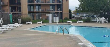 A swimming pool with lounge chairs and a multi-story building in the background.