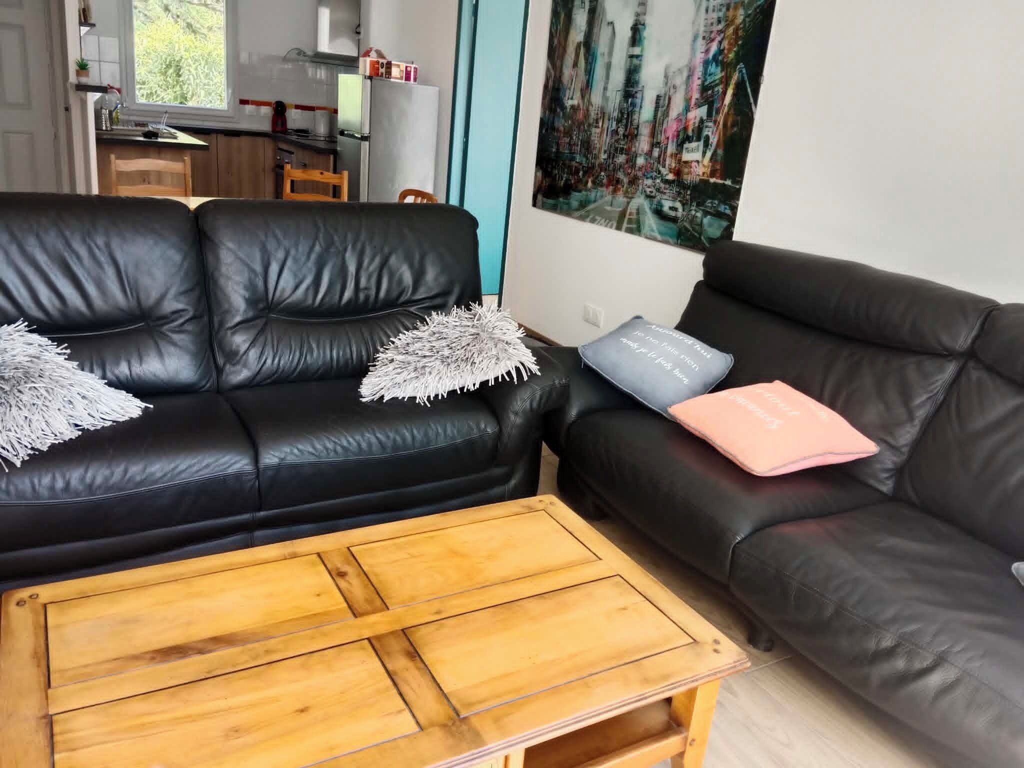 Ein Wohnzimmer mit einer schwarzen Ledersofa, einem Holztisch und einer Küche im Hintergrund.