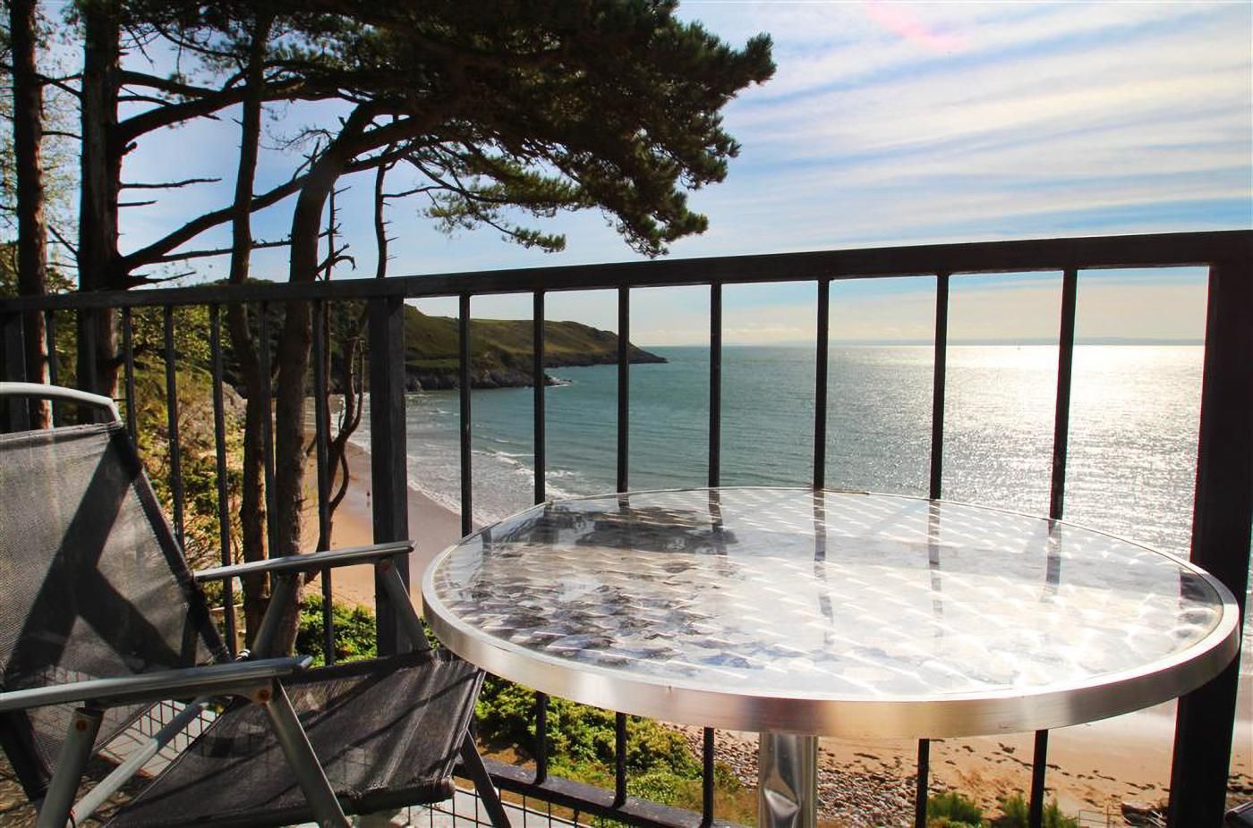Un balcón con mesa y sillas de vidrio, con vistas a la costa.