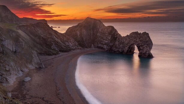 A coastal landscape with a prominent rock formation and a beach.