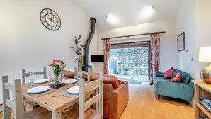A dining area with a wooden table set for four, a sofa, a TV, and a fireplace.