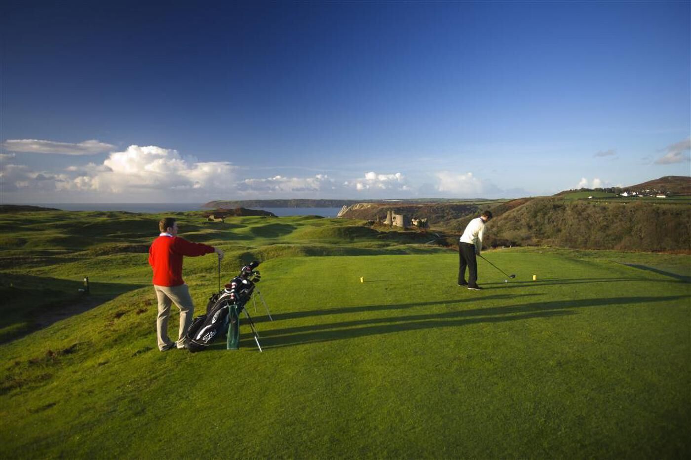 A golf course with rolling green hills, a clear sky, and a distant castle-like structure.