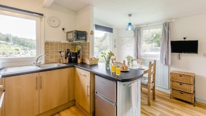 A kitchen with wooden cabinets, a microwave, a sink, and a dining area with a table and chairs. - 1 Bed in Caswell (oc-hh372) (Newton)
