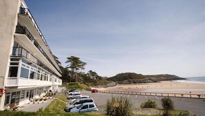 Un hotel sul lungomare con parcheggio, vista sulla spiaggia e un paesaggio collinare sullo sfondo.