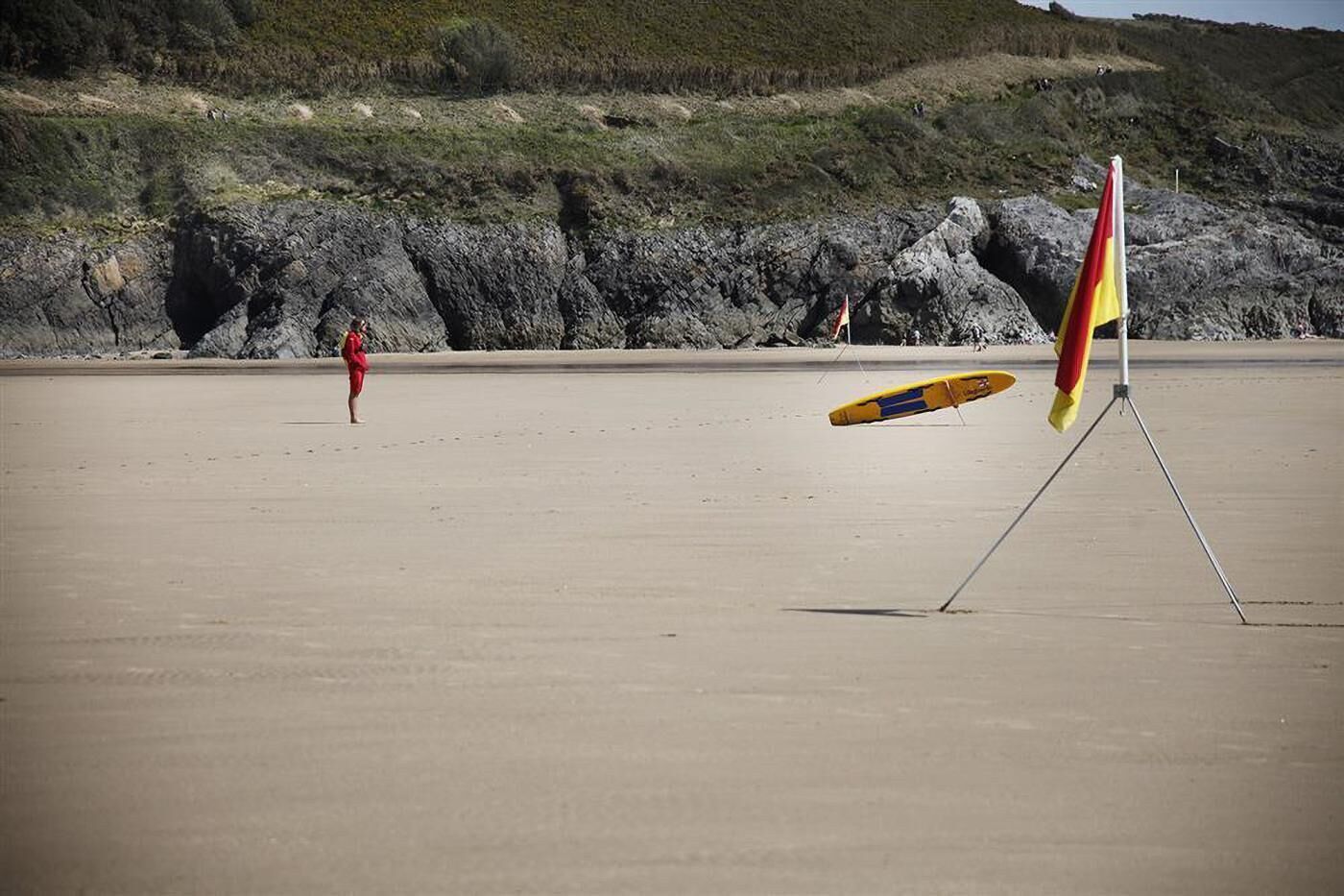 Una playa con un socorrista de rojo, una bandera y una tabla de surf.