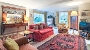 Een woonkamer met een rode bank, een fauteuil met een patroon, een salontafel, een televisie en een wandplank met decoratieve borden.