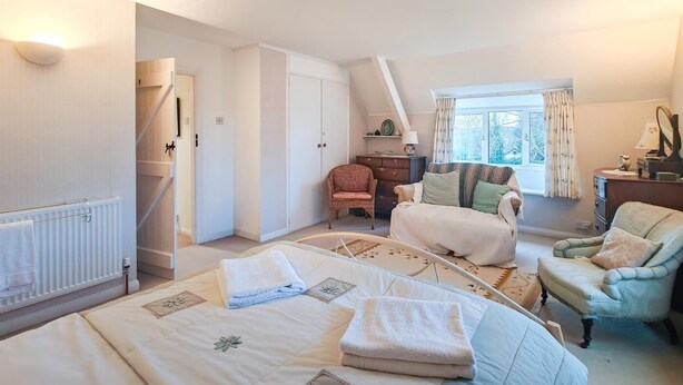 Een slaapkamer met een bed, twee stoelen, een dressoir, een radiator en een raam met gordijnen.